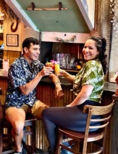 couple wearing hawaiian shirts, doing a cocktail cheers at Pupu House