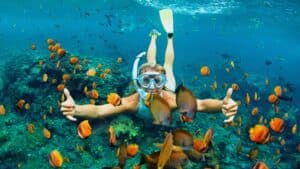 A girl throwing a shaka snorkeling underwater with orange fish