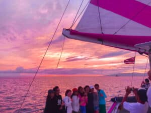 A group on a sunset cruise taking a photo in front of pink skies